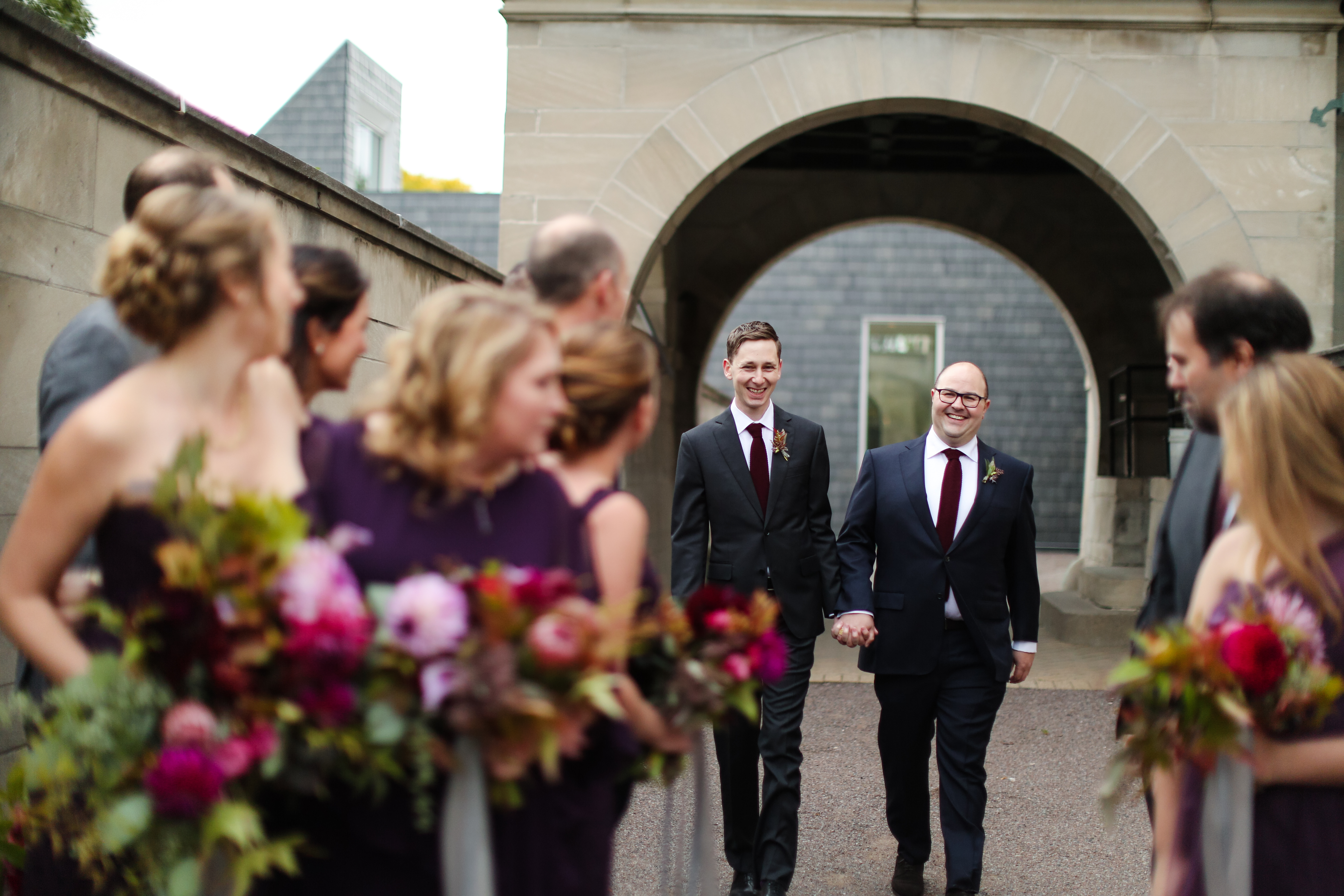 Grooms holding hands being greeted by the wedding party